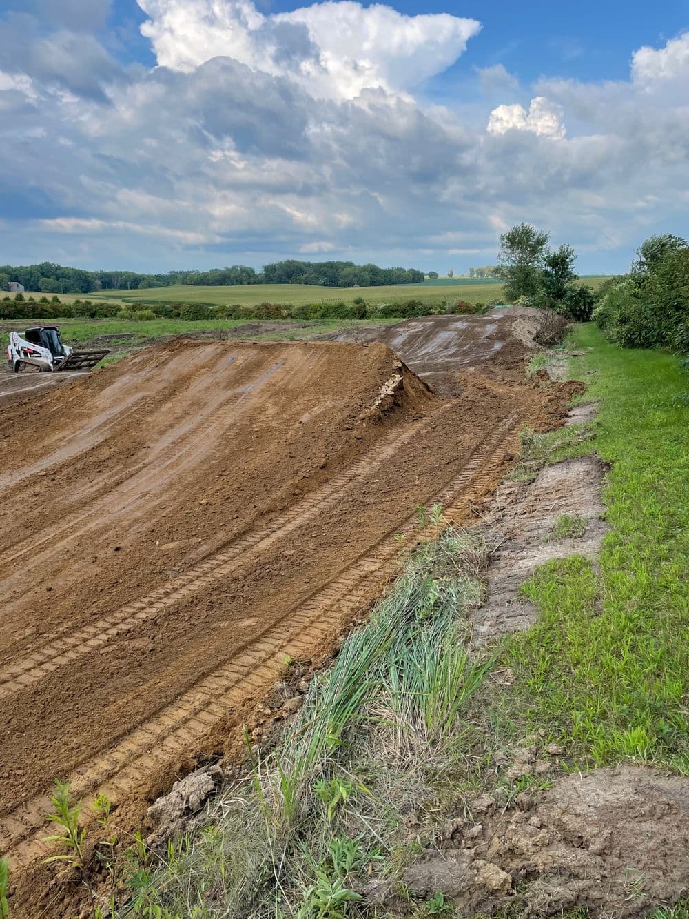 Construction site featuring freshly graded earth and machinery under a cloudy sky.
