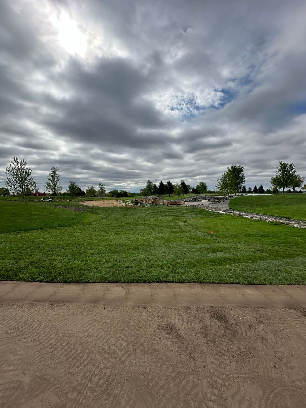 Cloudy skies over a green landscape with construction activity and trees in the background.