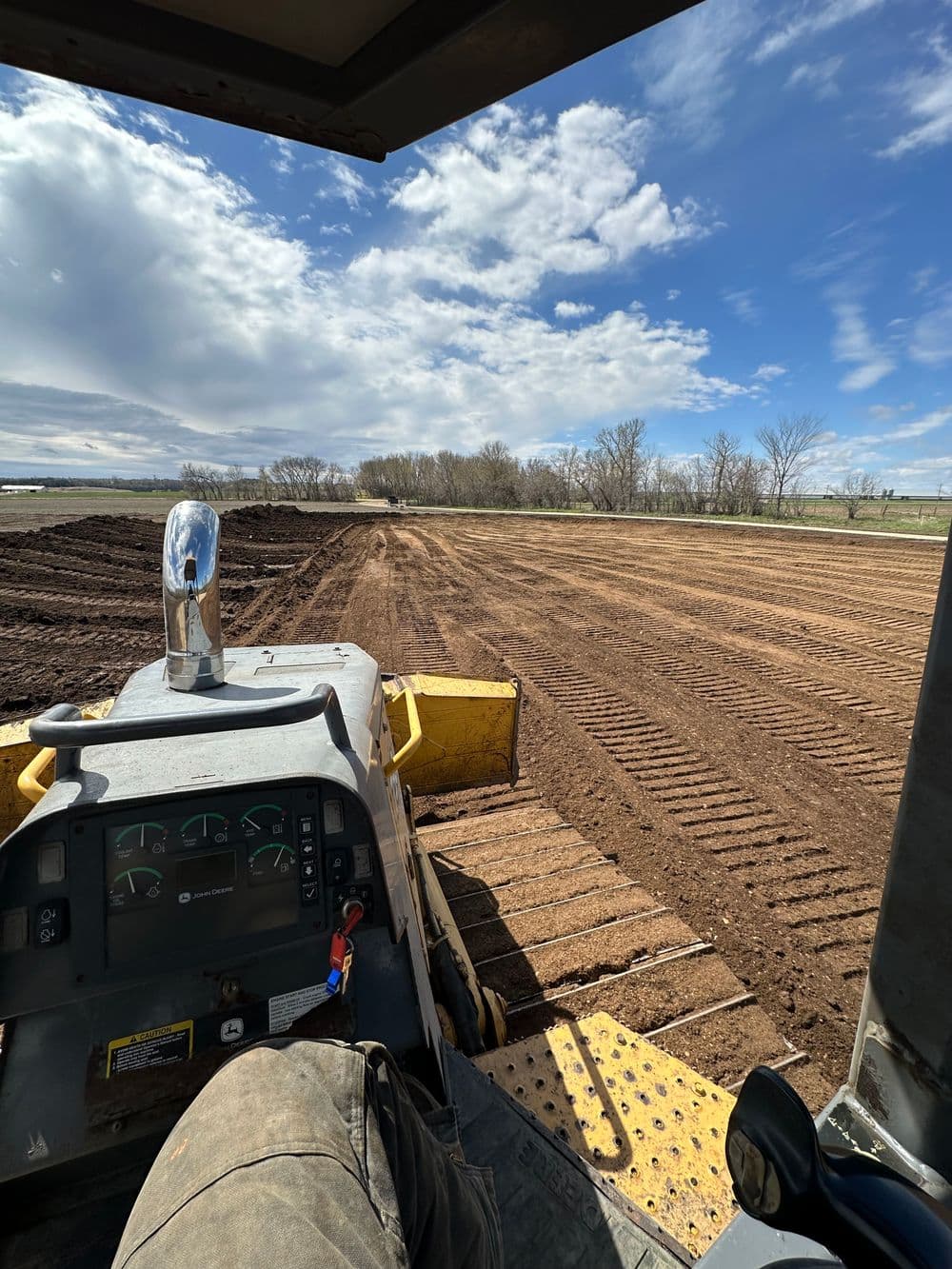 View from a tractor cabin overlooking freshly plowed farmland under a blue sky.