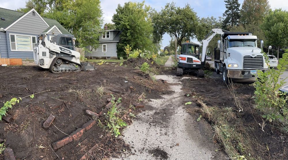 Construction equipment on residential street, with dirt and landscaping work in progress.